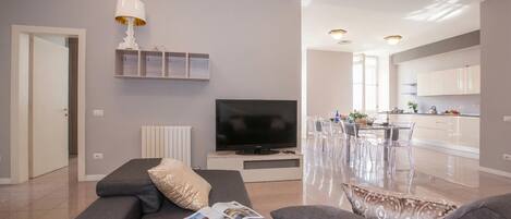 Una sala de estar moderna con un sofá, un televisor y un comedor con sillas transparentes.