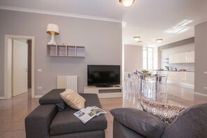 A modern living room with a sofa, a TV, and a dining area with transparent chairs. - Casa Daniele (Menaggio)