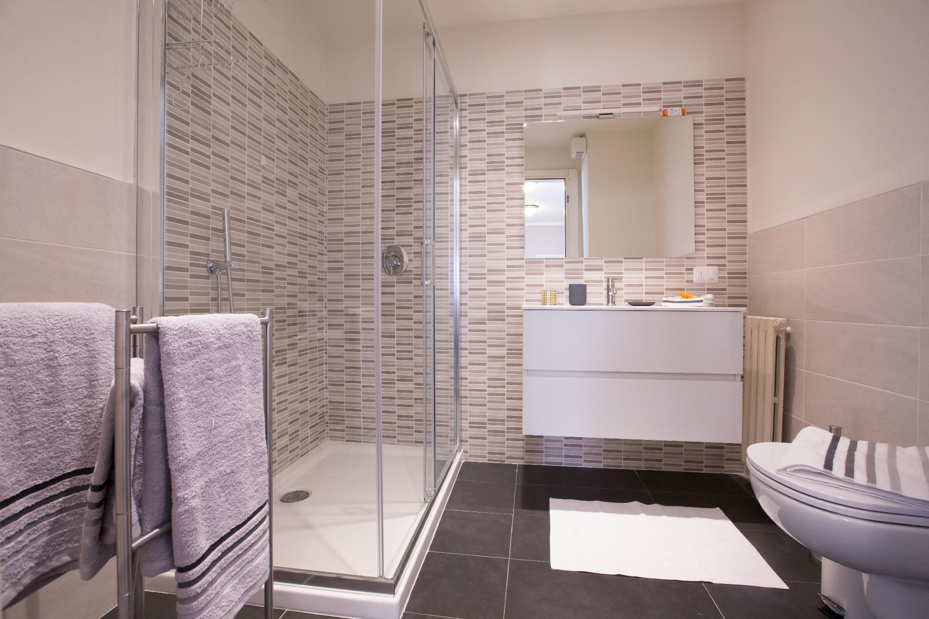 A modern bathroom with a glass-enclosed shower, a white sink, and a large mirror.