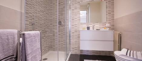A modern bathroom with a glass-enclosed shower, a white sink, and a large mirror.