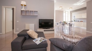 A modern living room with a sofa, a TV, and a dining area with transparent chairs. - Casa Daniele (Menaggio)
