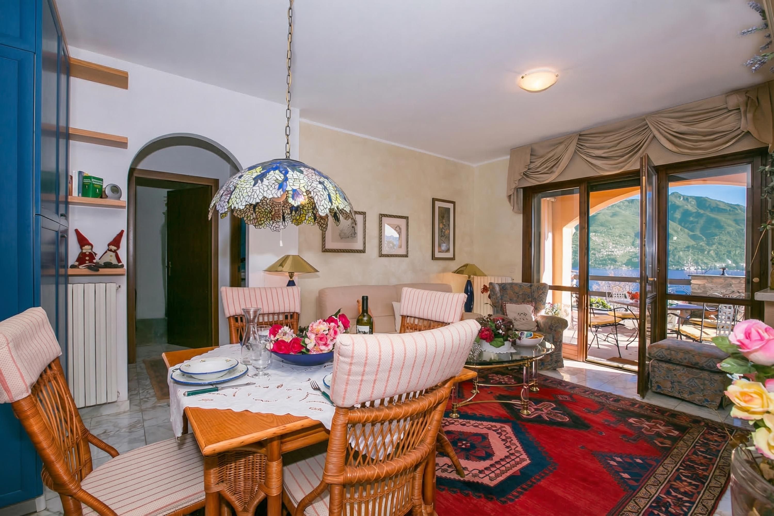 A dining area with wicker chairs, a table set with plates, a chandelier, and a view through a glass door.