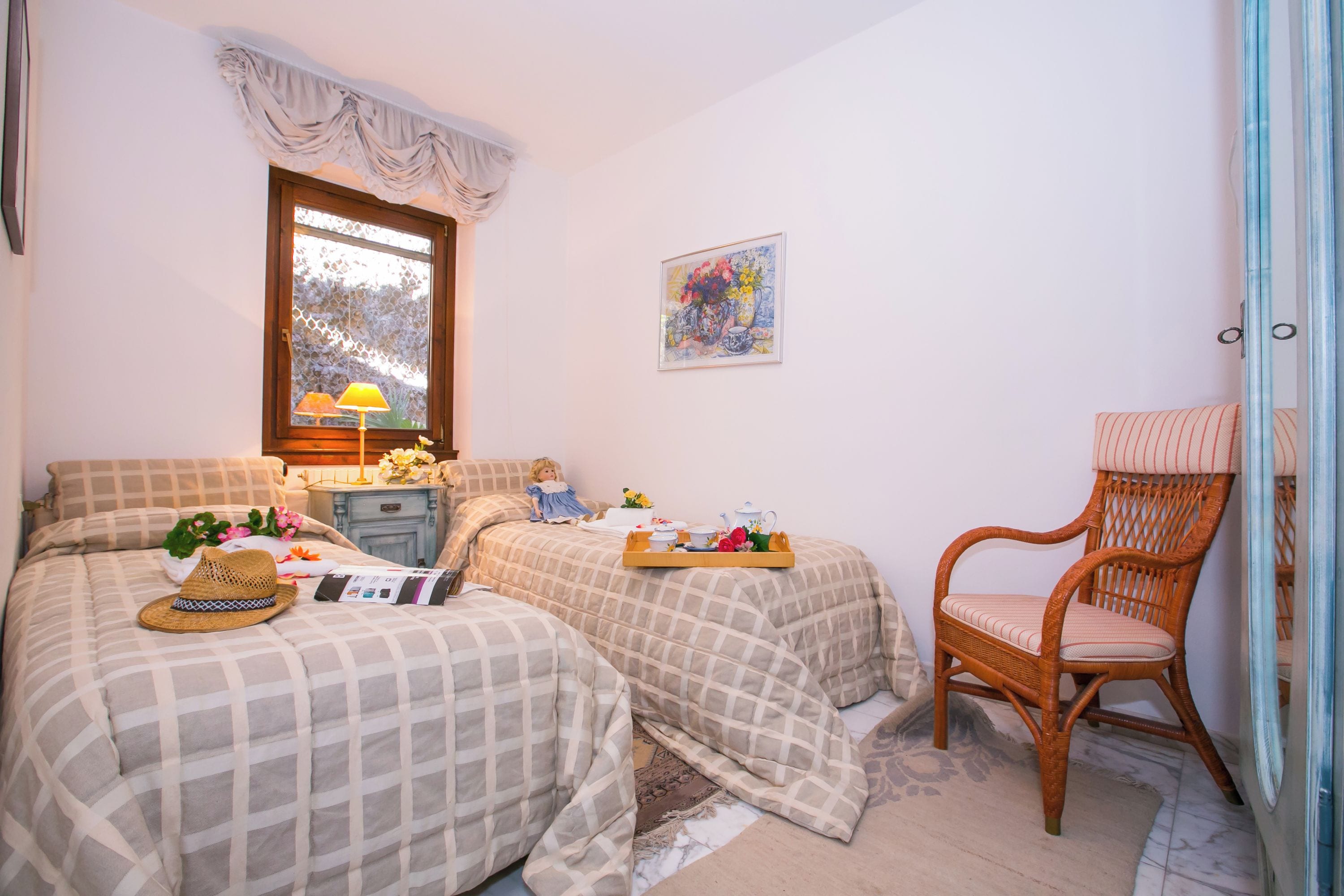 Una camera da letto con due letti, una finestra, una sedia e un quadro appeso al muro.