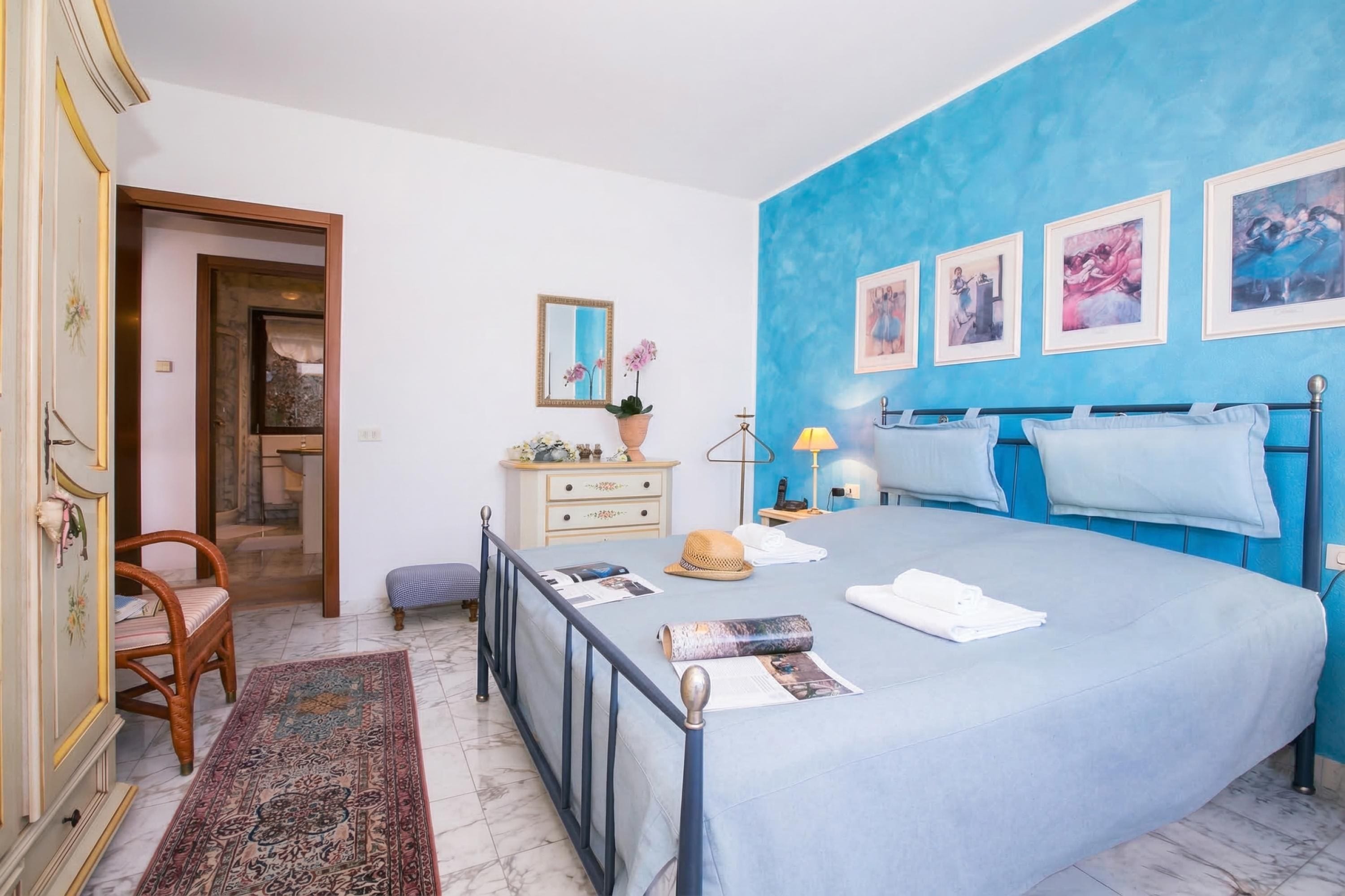A bedroom with a bed, a dresser, a chair, a rug, and artwork on the wall.