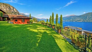 A house with a red roof, a well-maintained lawn, and a view of a lake and mountains. - Villa San Michele (Griante)