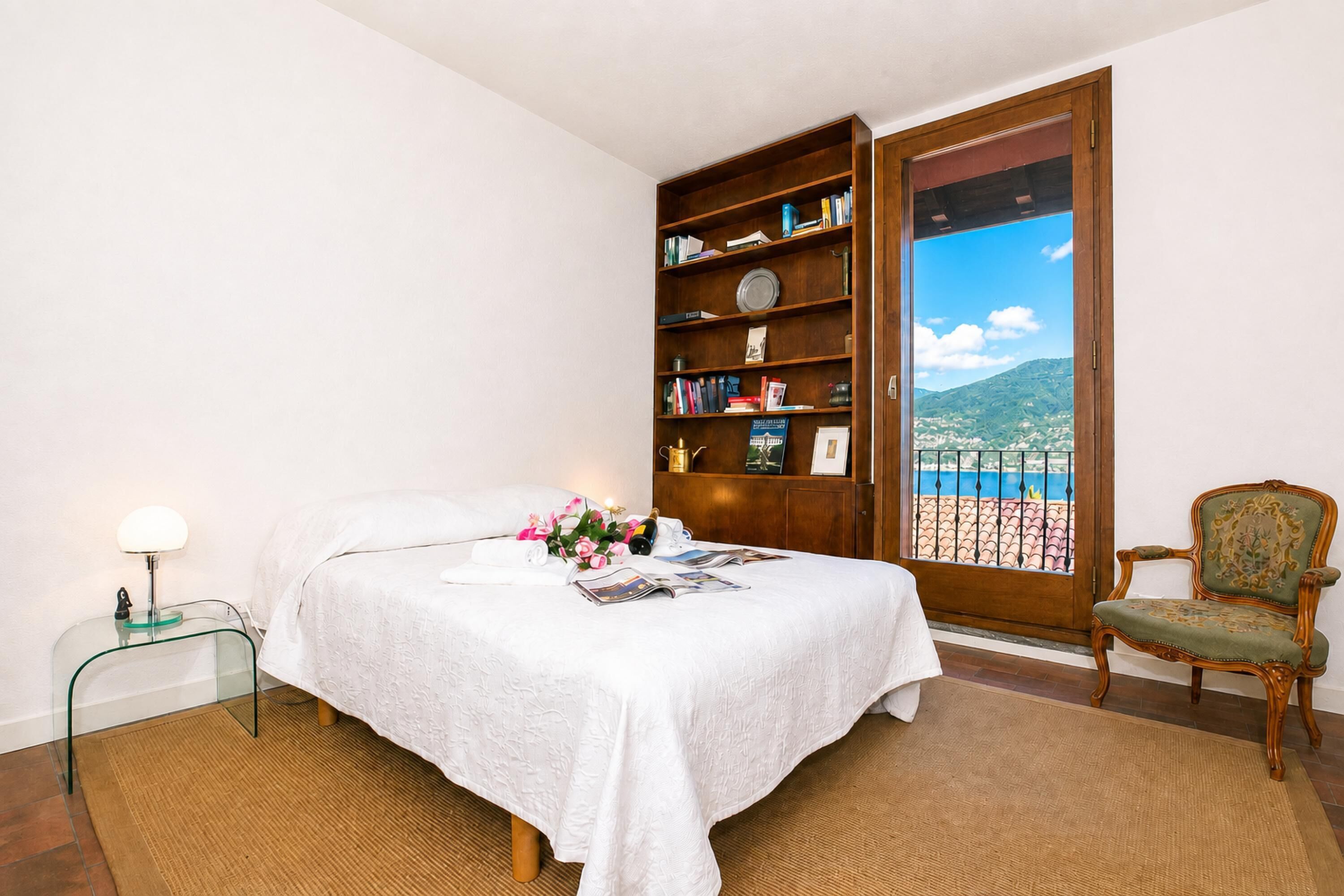 A bedroom with a bed, a bookshelf, a chair, and a view through a door.