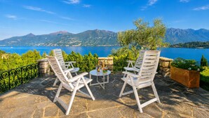 An outdoor seating area with stone flooring, white chairs, and a table. - Villa San Michele (Griante)