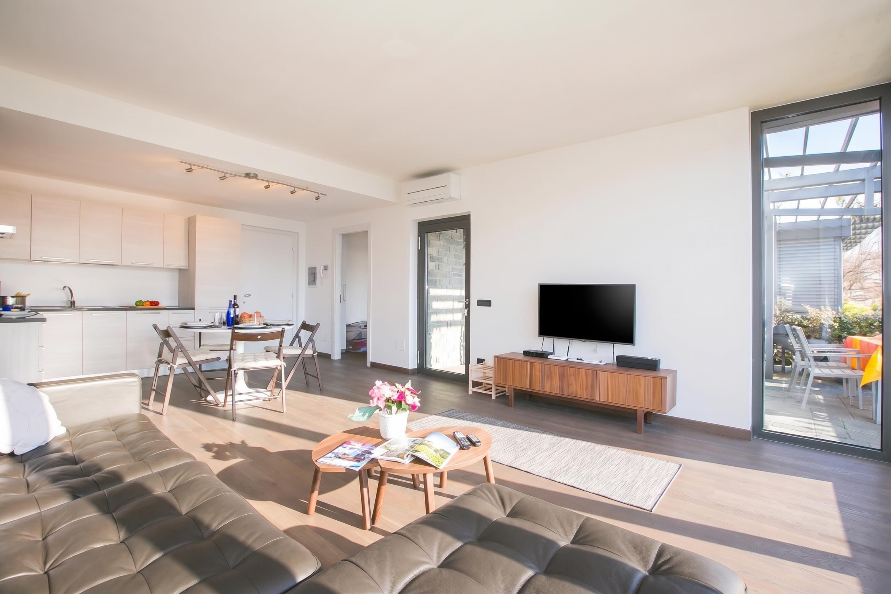 Una sala de estar moderna con un sofá, una mesa de centro y un televisor. Hay una zona de cocina con armarios y una mesa de comedor.