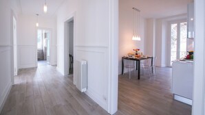 Una cuina moderna amb armaris blancs, una zona de menjador amb taula i cadires, i un passadís amb paviment de fusta i parets blanques.
