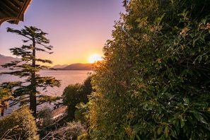 Un paisaje costero con un atardecer, montañas a lo lejos y una vegetación densa.