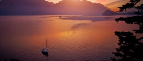 A calm lake with a boat, mountains in the background, and trees framing the scene.