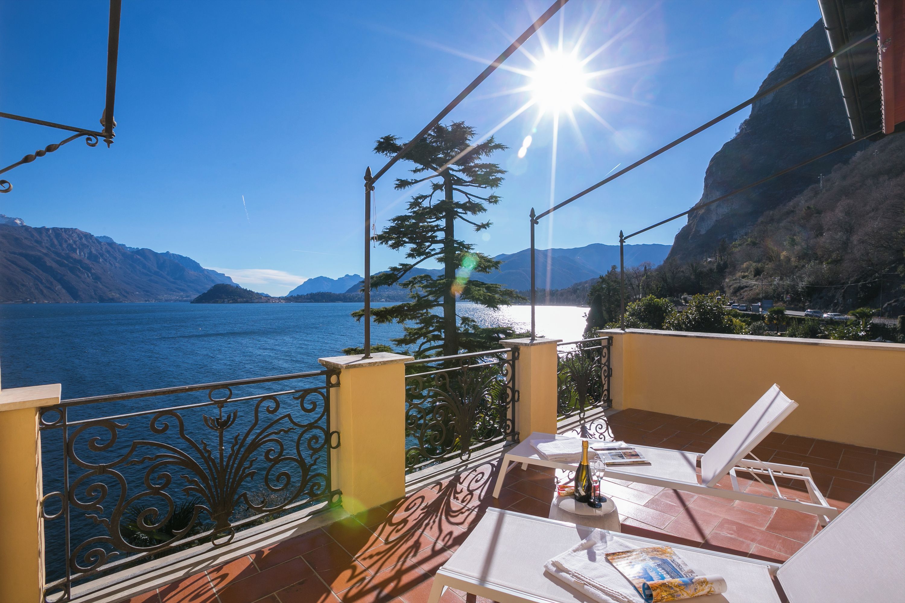 A balcony with a view of the sea, a table with chairs, and a bottle of wine.