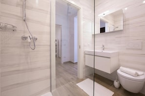 Un baño moderno con cabina de ducha de vidrio, un lavamanos blanco y un inodoro.