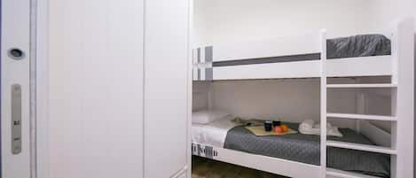 Un lit superposé avec un matelas gris et une armoire blanche à porte.