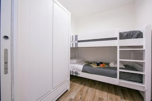 Una cama litera con colchón gris y un armario blanco con puerta.