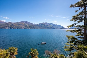 A calm lake with a sailboat, surrounded by mountains and palm trees. - Villa Evelyn Terrazzo (Menaggio)