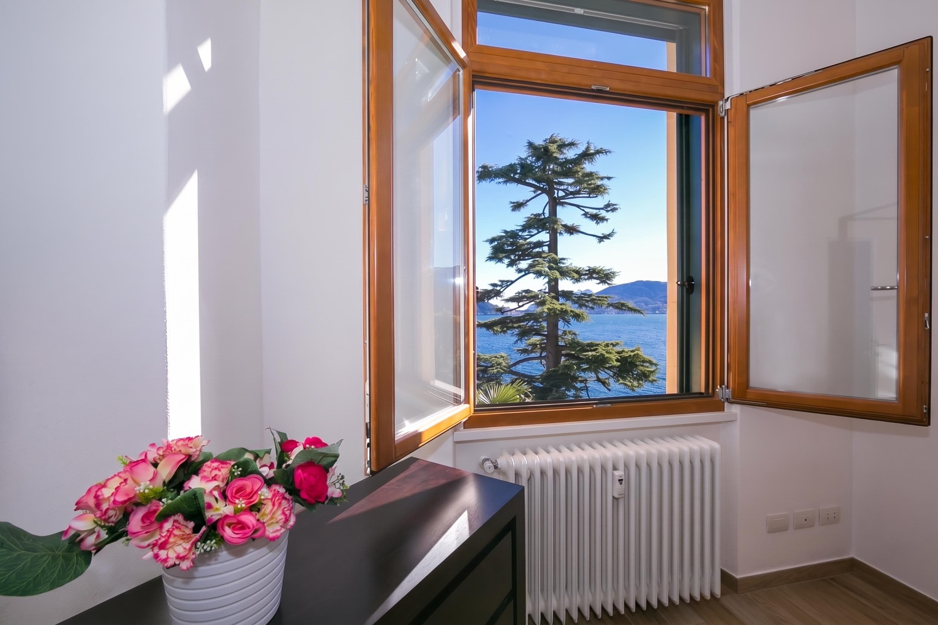 A room with a large window, a radiator, and a vase with flowers on a table.