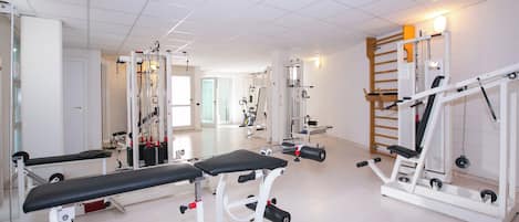 Un gimnasio con equipo de ejercicio, bancos y un espejo grande.