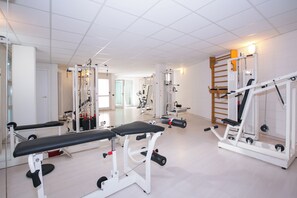 Un gimnasio con equipo de ejercicio, bancos y un espejo grande.