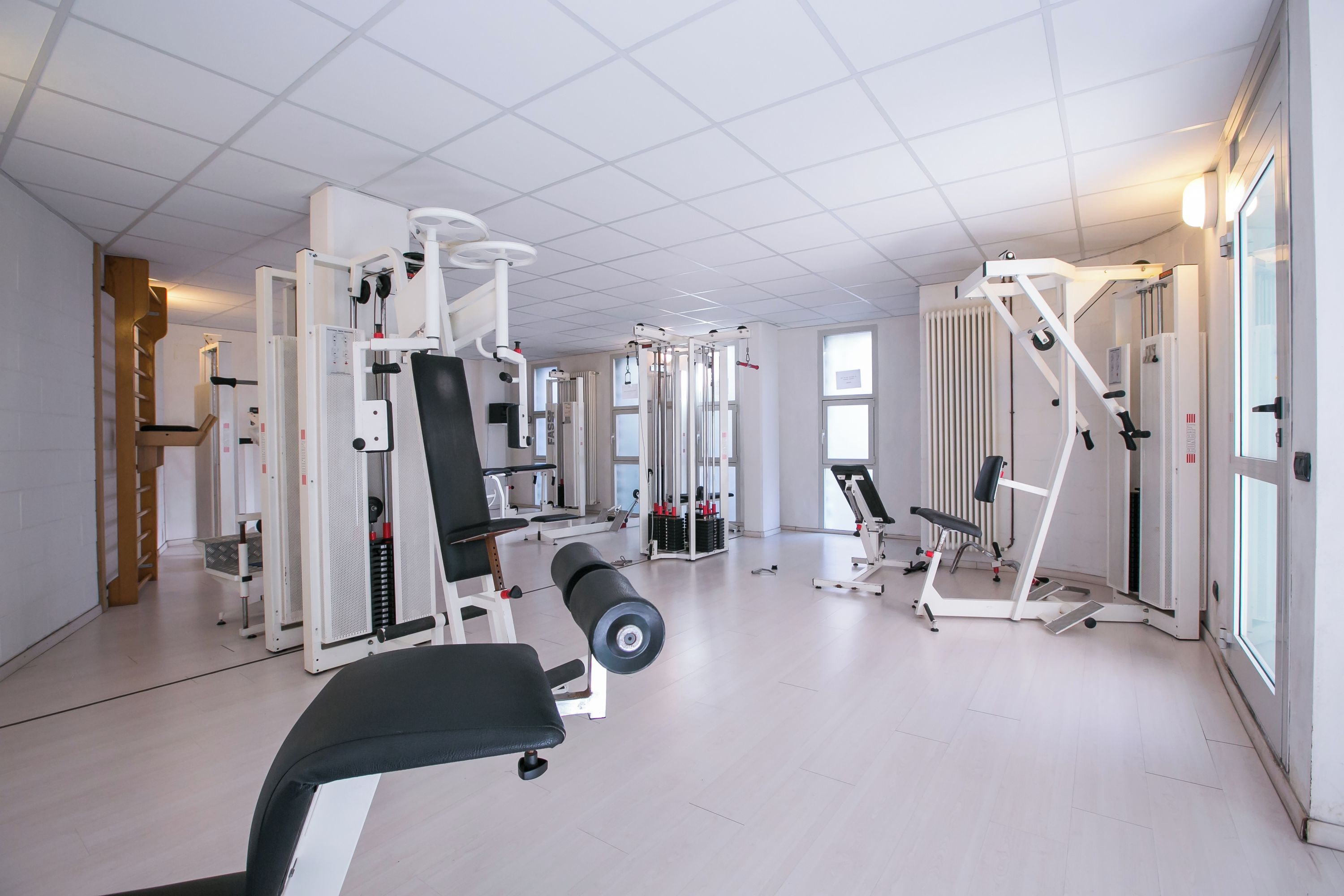 A gym with various exercise machines, a bench, and a mirrored wall.