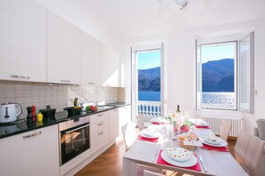 A modern kitchen with white cabinets, a black countertop, and a dining area set for a meal. - Villa Larius Balcone (Carate Urio)