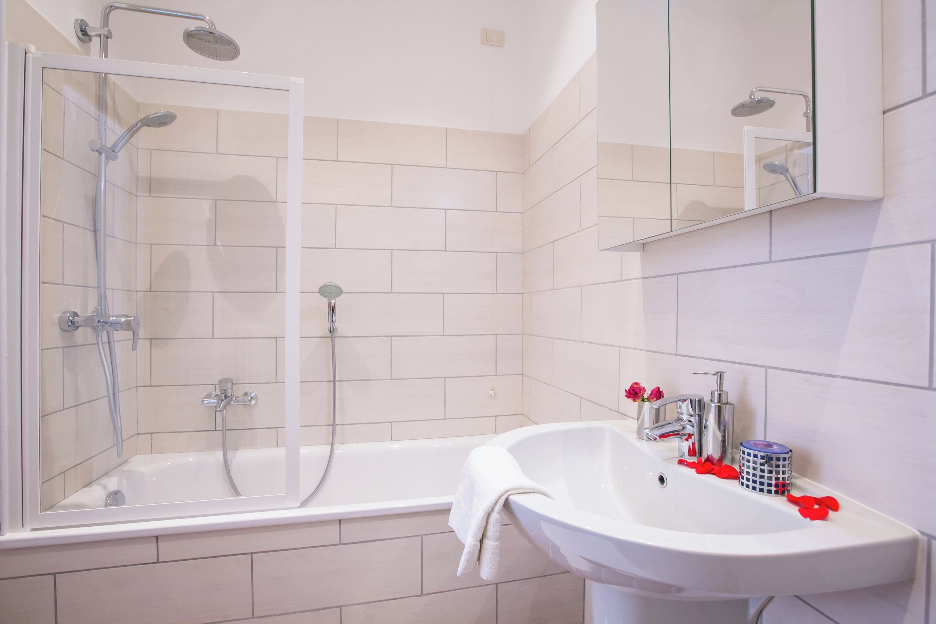 A modern bathroom with a glass-enclosed shower, a white bathtub, and a sink with a mirror above it.