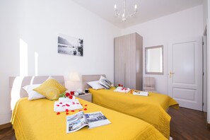 A hotel room with two beds, a bedside table with a lamp, a wall-mounted picture, and a door. - Villa Larius Balcone (Carate Urio)