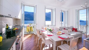A modern kitchen with a view of the sea, a dining area with a table set for four, and a living area with a sofa and a balcony. - Villa Larius Balcone (Carate Urio)