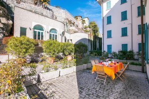 A courtyard with a table set for dining, surrounded by potted plants and a stone wall. - Villa Larius Balcone (Carate Urio)