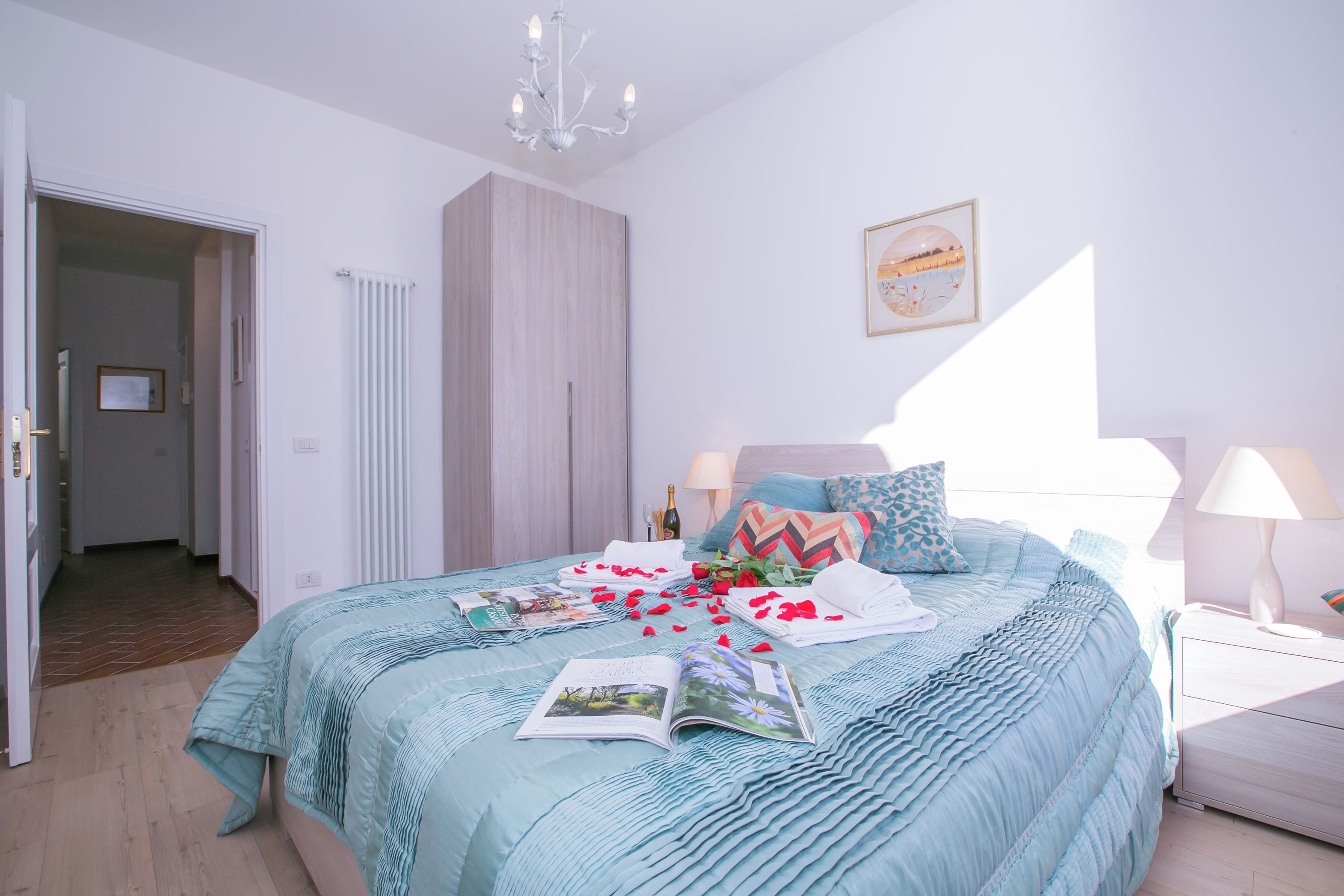 Een slaapkamer met een bed, een kledingkast, een nachtkastje, een lamp en een kroonluchter.