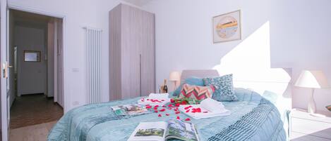 Een slaapkamer met een bed, een kledingkast, een nachtkastje, een lamp en een kroonluchter.