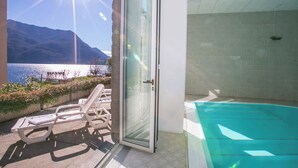 A balcony with a glass door leading to a swimming pool, a lounge chair, and a view of a lake and mountains. - Villa Larius Balcone (Carate Urio)