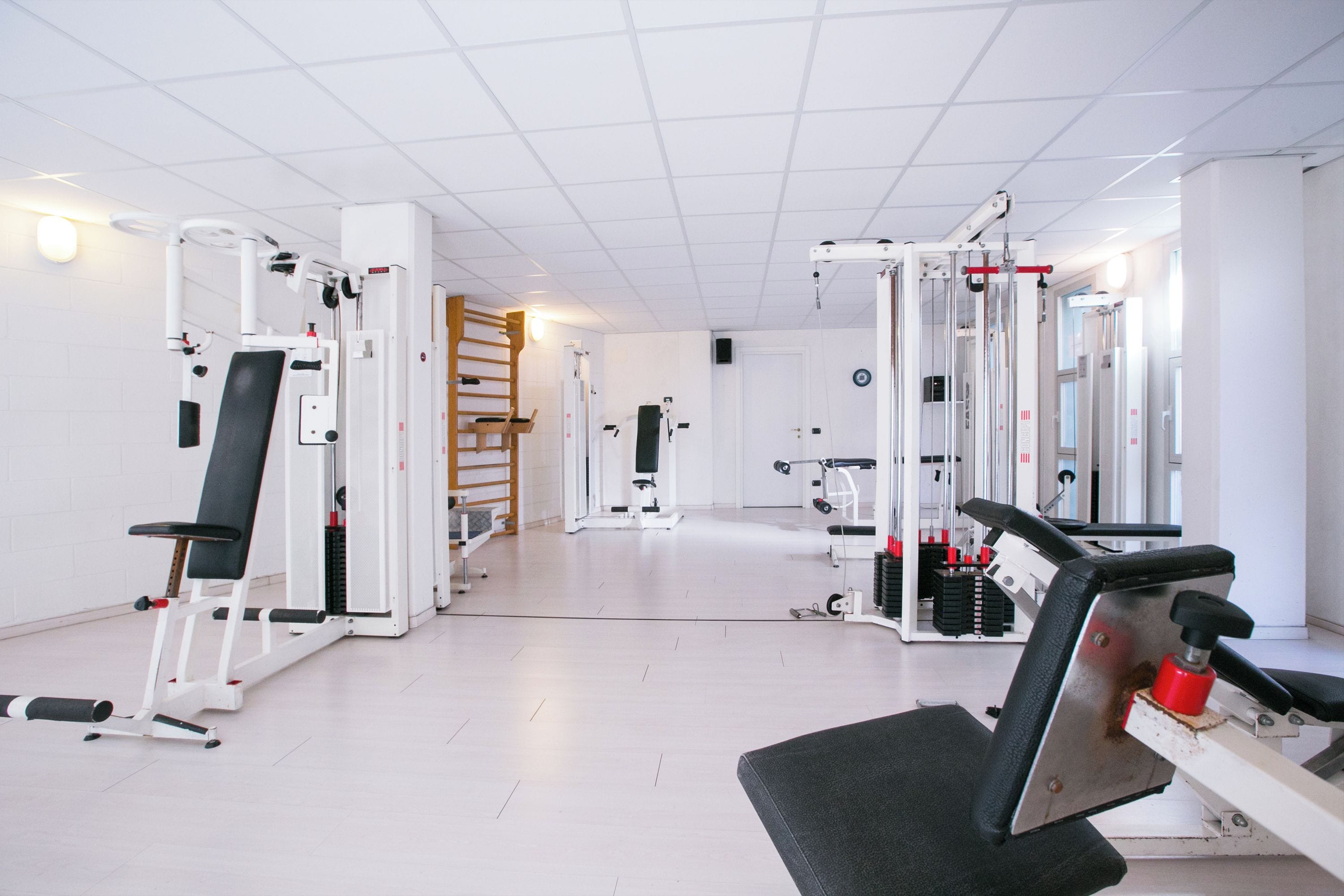 Une salle de sport équipée de divers appareils d’exercice, d’une échelle en bois et d’une porte donnant sur une autre pièce.