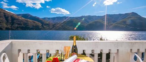 A balcony with a table set for a celebration, overlooking a lake and mountains.