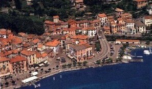 An aerial view of a coastal town with buildings clustered around a central street, leading to a waterfront area with boats. - Villetta Argegno (Argegno)