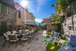 An outdoor patio with stone flooring, a round table with chairs, and a small seating area with a table and chairs. - Villetta Argegno (Argegno)
