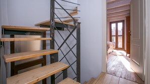 Una escalera con escalones de madera y barandillas de metal, que lleva a una habitación con piso de madera y una puerta.