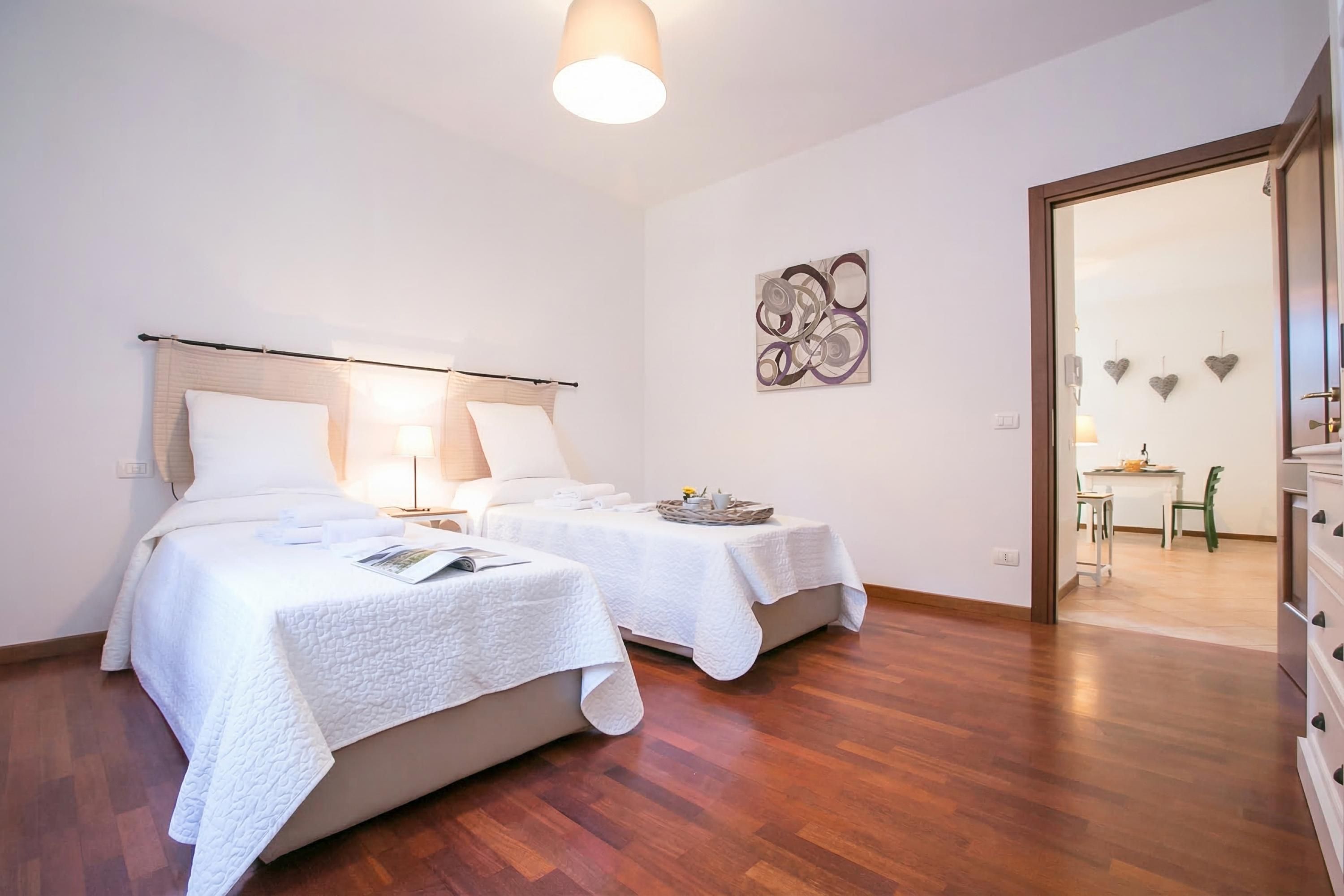 A hotel room with two beds, a dining area, and a hallway.