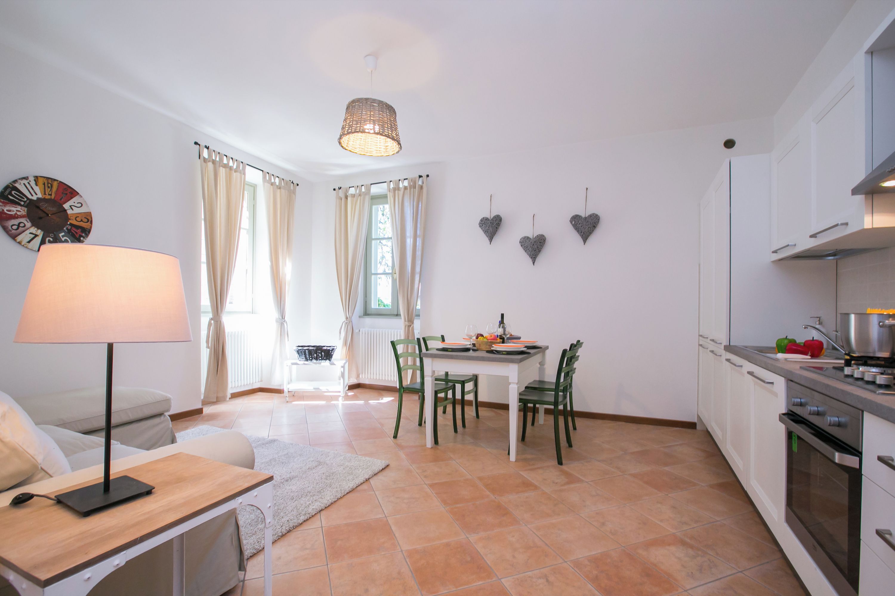 A modern kitchen with white cabinets, a dining table with chairs, a lamp, and a clock on the wall.