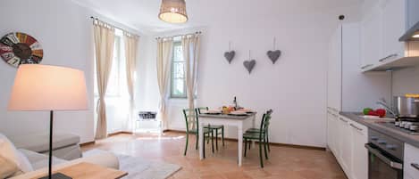 A modern kitchen with white cabinets, a dining table with chairs, a lamp, and a clock on the wall.