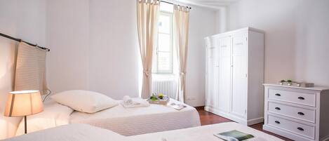 A hotel room with two beds, a wardrobe, a lamp, and a window with curtains.