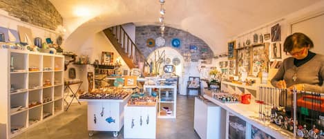 An interior with a stone archway, shelves with various items, and a person working at a counter.