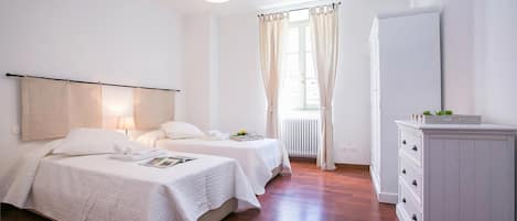 Une chambre avec deux lits, une table de chevet avec une lampe, une commode et une fenêtre avec des rideaux.