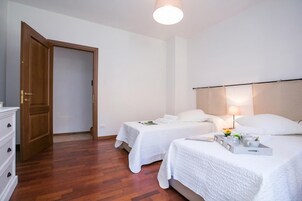 A hotel room with two beds, a wooden door, a white dresser, and a bedside table with a lamp.