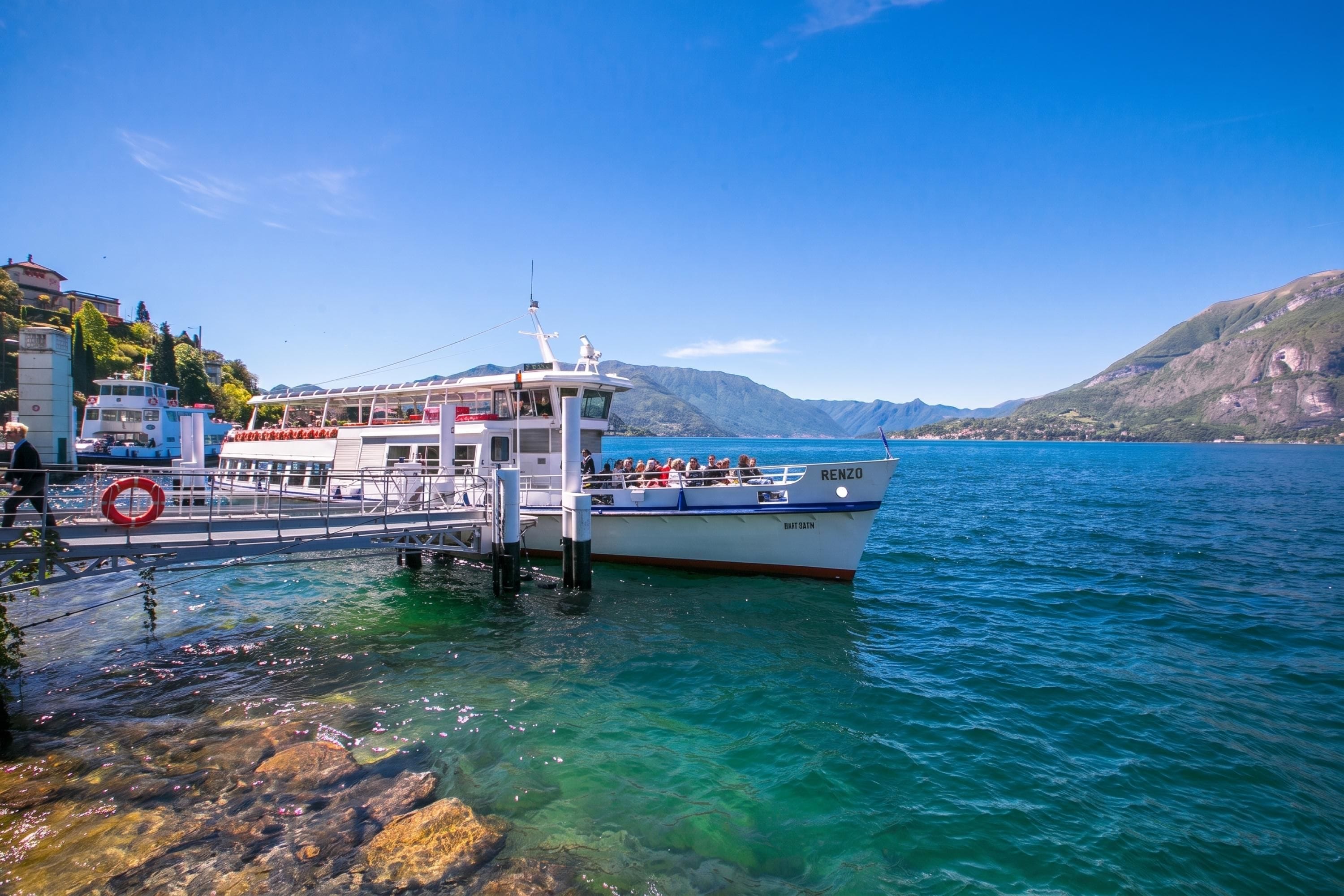 A boat docked at a pier with clear water and mountains in the background.