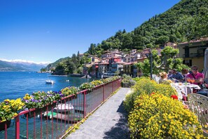 A lakeside walkway with a red railing, surrounded by colorful flowers and buildings with balconies. - Casa Al Prato Apt. B (Varenna)