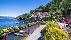 Un passeig al costat del llac amb una barana vermella, envoltat de flors de colors i edificis amb balcons.