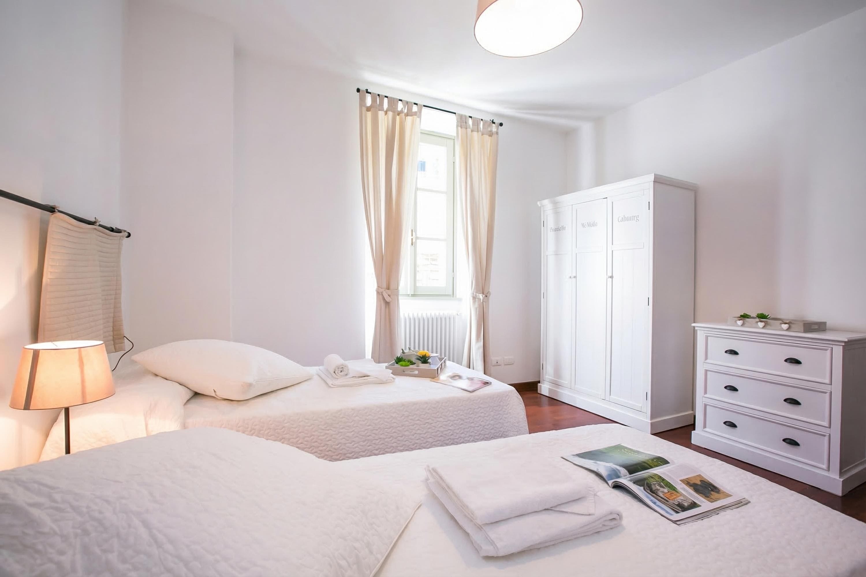 Ein Hotelzimmer mit zwei Betten, einem Schrank, einer Lampe und einem fenster mit Vorhängen.