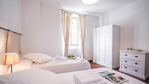 Habitació d'hotel amb dos llits, un armari, una làmpada i una finestra amb cortines.