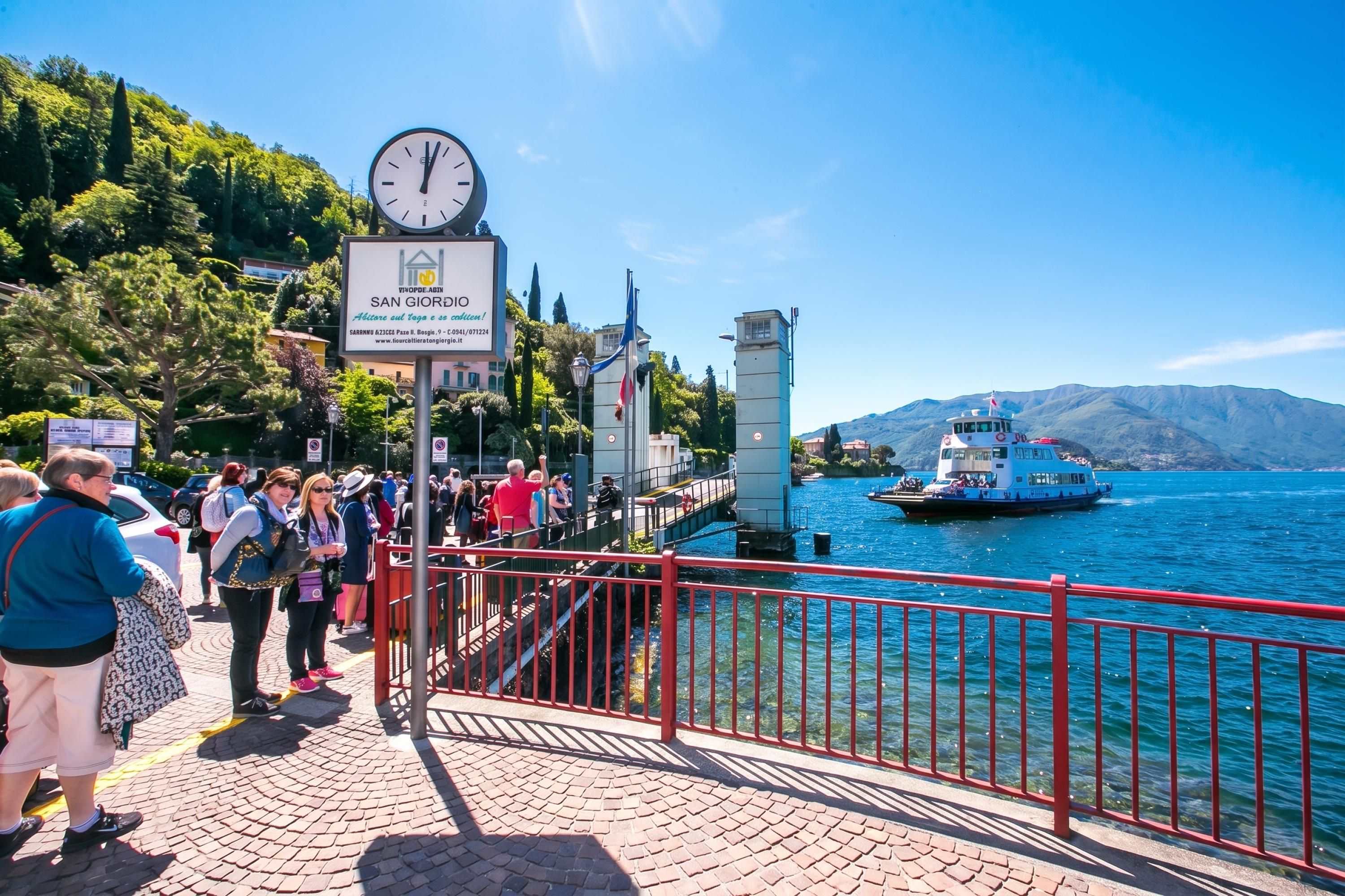 A waterfront promenade with a clock, a signboard, and a boat in the background.